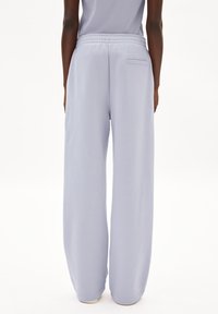 Pantalones de pierna ancha de lavanda clara, confeccionados con tela suave. Cuentan con una cinturilla elástica y un bolsillo trasero. Textura lisa con un corte relajado.