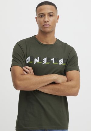 Olivgrünes Baumwoll-T-Shirt mit kurzen Ärmeln, das ein kräftiges, abstraktes Grafikdesign in Schwarz und Weiß mit grünen Akzenten zeigt.