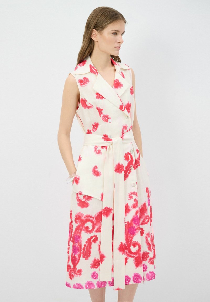 Ärmelloses Leinenkleid mit fließender Silhouette, besitzt einen hellcremefarbenen Grund mit kräftigen roten Blumenmustern, tailliert mit einem Gürtel und seitlichen Taschen.