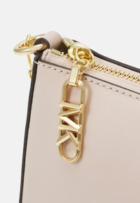 Angolo di borsa in pelle rosa con zip dorata, catena e un accento dorato con logo geometrico. Texture liscia, design minimalista.