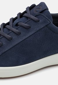 Navy blue leather sneaker with textured surface, round toe, and flat laces; features a white rubber sole and subtle logo on the tongue.