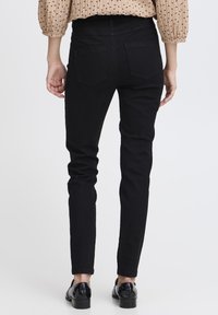 Jean skinny noir en denim ; avec deux poches arrière et une coupe slim, associés à des chaussures noires brillantes.