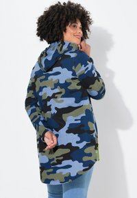 Felpa con cappuccio a motivo camouflage nei toni del blu, verde e nero. Maniche lunghe, orlo curvo e dettagli zip di un brillante verde. Tessuto morbido.