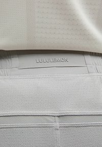 Lichtgrijze sportbroek met een gestructureerde stof, mesh accenten en een zichtbare, merkgebonden tailleband die aan de bovenkant is gestikt.