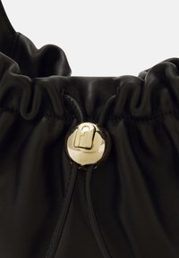 Musta nahkainen nyörilaukku, jonka yläosa on kerätty yhteen ja jossa on kultainen metallinen lukko ja sileä pinta. Yksinkertainen muotoilu, ei näkyviä kuvioita.