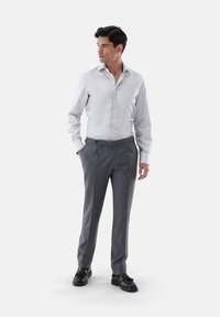 Hellgrau gestreiftes Hemd mit Button-Down-Kragen und durchgehender Knopfleiste, kombiniert mit dunkelgrauen maßgeschneiderten Hosen und schwarzen Lederschuhen.