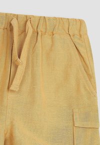 Lyse gule shorts i tekstureret stof, med elastisk talje, snoretræk og sidelommer. Har stikninger og en cargo-lomme.