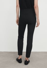 Leggings noirs élastiques au design ajusté et à la texture lisse, se terminant juste au-dessus de la cheville. Portés avec des chaussures noires à enfiler texturées.