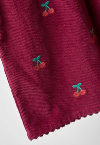 Bordeaux stof met ribbelstructuur, voorzien van kleine geborduurde kersenmotieven in oranje en groen, afgewerkt met een geschulpt randje.