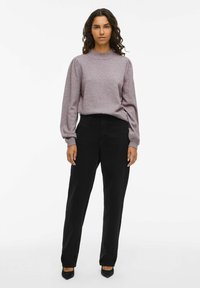 Maglione lavorato a maglia viola chiaro con maniche a sbuffo abbinato a pantaloni neri a vita alta e décolleté neri a punta. Sfondo bianco semplice.