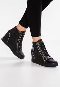 Black wedge sneakers with textured black leather upper, lace closure, silver accents, and a logo detail on the side.