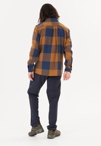 Brun och blå plaidskjorta med lång ärm, lös passform och spetsig krage, kombinerad med marinblå byxor och bruna vandringsskor.