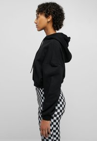 Svart hettegenser med en avslappet passform og snorfestet hette, kombinert med høyt liv leggings som har et svart-hvitt rutemønster.