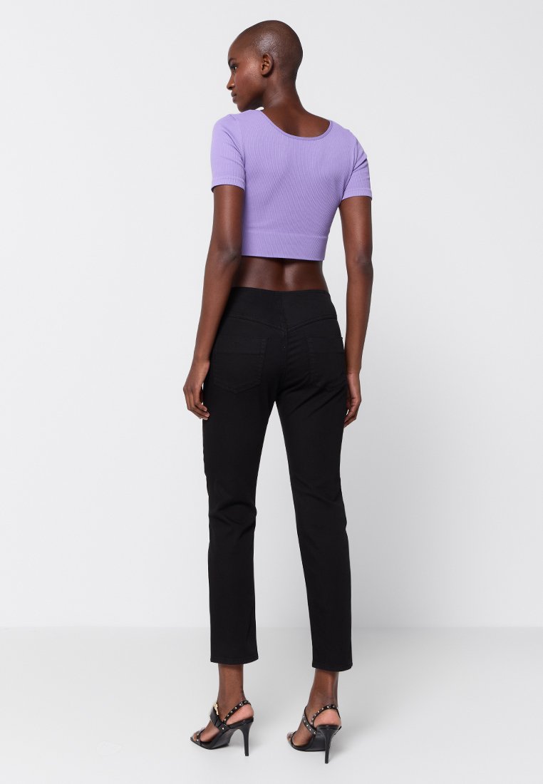 Czarne dopasowane dżinsy i prążkowany, liliowy krótkotali bluzka. Bluzka ma krótkie rękawy i okrągły dekolt. Modelka nosi czarne sandały na obcasach z paskami.