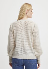 Pull en tricot beige clair avec des motifs diagonaux et des manches bouffantes. Présente un ourlet côtelé et une texture en maille ouverte pour la respirabilité.