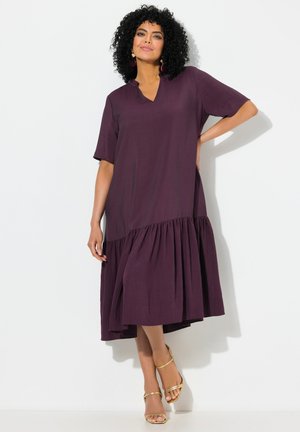 Lila, kurzärmliges Kleid mit V-Ausschnitt und gestuftem Saum, aus leichtem Stoff; kombiniert mit goldenen Sandalen.