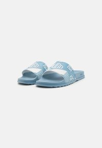 Ciabatte slide azzurre con una suola testurizzata, dotate di una fascia bianca con motivi geometrici e logo del brand. Materiale sintetico morbido.