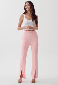 Lichtroze getailleerde broek met zijsplitsen, een zachte textuur en een hoge tailleband, gecombineerd met een aansluitend wit geribbeld hemdtop.
