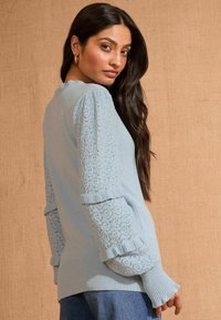 Svetlo modri pulover z enotno oblačilom, zapletenimi pufastimi rokavi iz čipke ter rebrastimi manšeti in robom.