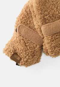 Beige flis rokavice z teksturirano, puhasto površino in Velcro zapiranjem. Imajo rjavo oznako z logotipom "The North Face".