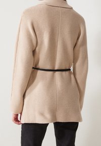 Beige strukturierter Cardigan mit Kragen, tailliert mit einem schwarzen Gürtel. Verfügt über lange Ärmel und einen geraden Schnitt am Saum.