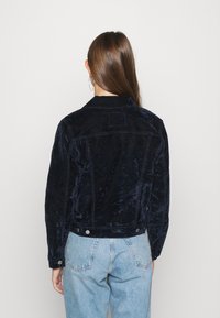 Giacca in velluto a coste blu navy con una finitura morbida e testurizzata. Presenta un colletto classico, una spalla posteriore e dettagli in metallo argentato.