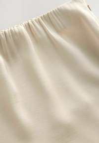 Jasnobeżowa tkanina o gładkiej fakturze, z elastycznym pasem w talii i delikatnym połyskiem. Minimalistyczny design bez widocznych wzorów czy akcentów.