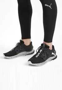 Baskets de sport noires avec une tige en mailles, une semelle noire texturée et une semelle intermédiaire à éclats blancs ; lacets et détails du logo en noir.