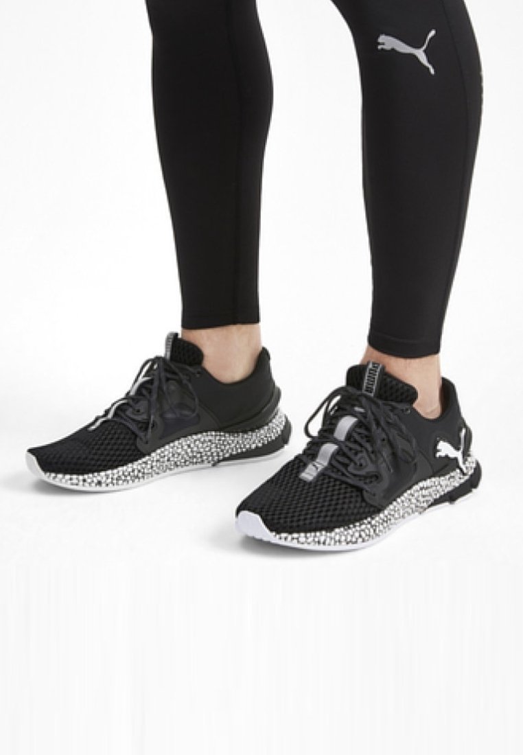 Baskets de sport noires avec une tige en mailles, une semelle noire texturée et une semelle intermédiaire à éclats blancs ; lacets et détails du logo en noir.
