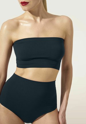 Femme portant un haut bandeau noir sans bretelles et des sous-vêtements taille haute, montrant le haut du torse et le visage partiellement tourné.