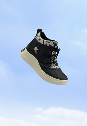 Zapatilla alta en blanco y negro con parte superior estampada, cordones negros, suela crema y un parche de logo en el lateral sobre un fondo de cielo azul.