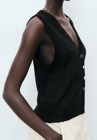 Chaleco negro corto hecho de tejido de punto, con grandes sisas, escote en V y tres botones metálicos en la parte delantera.