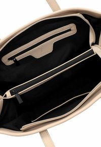 Interno di una borsa in pelle beige con rivestimento in tessuto nero. Presenta una tasca con zip e due scomparti aperti per l'organizzazione.
