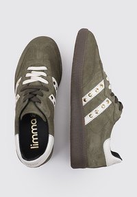 Zapatillas de ante verde con rayas blancas y tachuelas de latón. Presentan una puntera redondeada, cierre de cordones y suela de goma marrón texturizada.