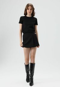 Zwarte aansluitende T-shirt gecombineerd met een zwarte minirok met een goudkleurig accent. Model draagt kniehoge zwarte laarzen. Soepele stoftextuur.