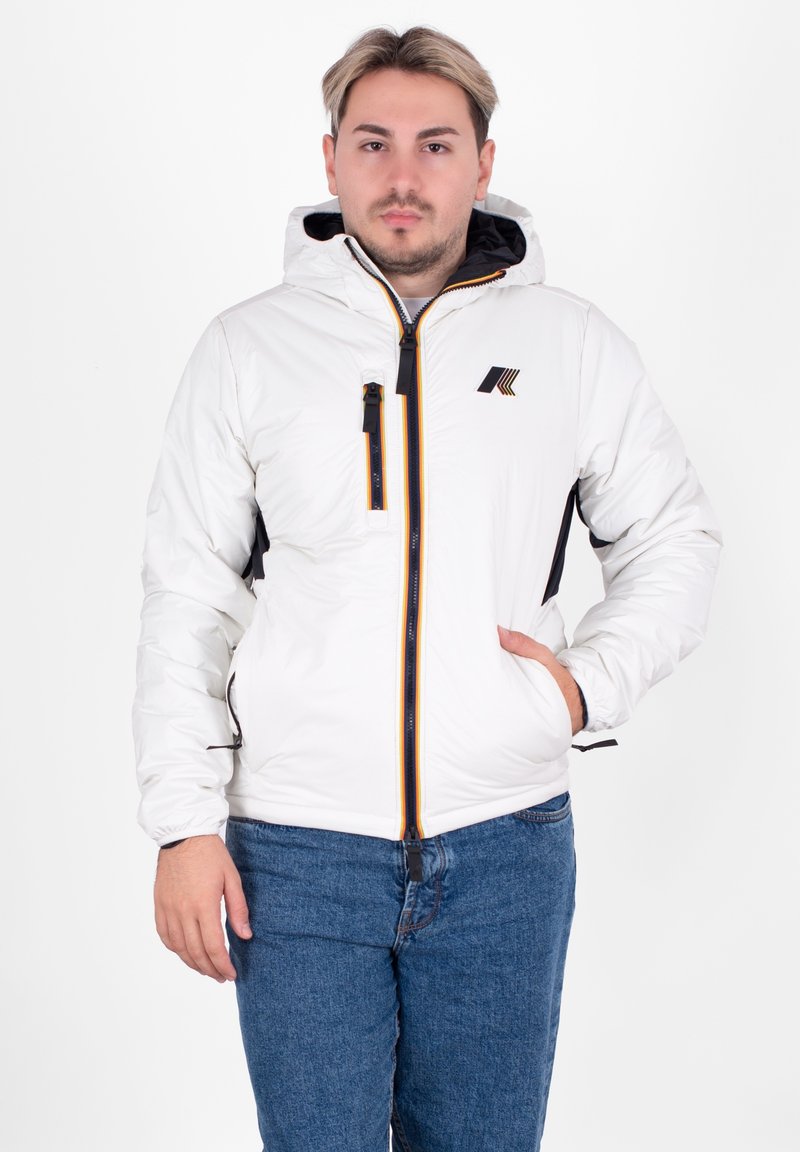 Biała pikowana kurtka z kapturem, z czarnym zamkiem błyskawicznym, żółtymi i pomarańczowymi akcentami oraz logo na piersi. Czarne boczne panele.