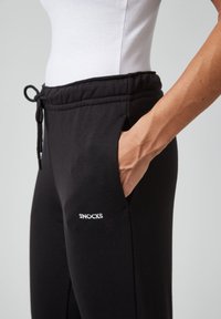Zwarte sweatpants van zacht materiaal, met een elastische tailleband met een trekkoord, zijzakken en het "SNOCKS" logo in het wit.
