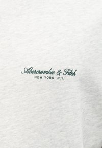 Λευκό ύφασμα με κεντημένο το "Abercrombie & Fitch NEW YORK, N.Y." σε σκούρο πράσινο με καλλιγραφικά και κεφαλαία γράμματα.