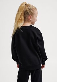 Svart sweatshirt med en bekväm passform, ribbade ärmslut och rundad halsringning. Tyget verkar mjukt med en slät textur.