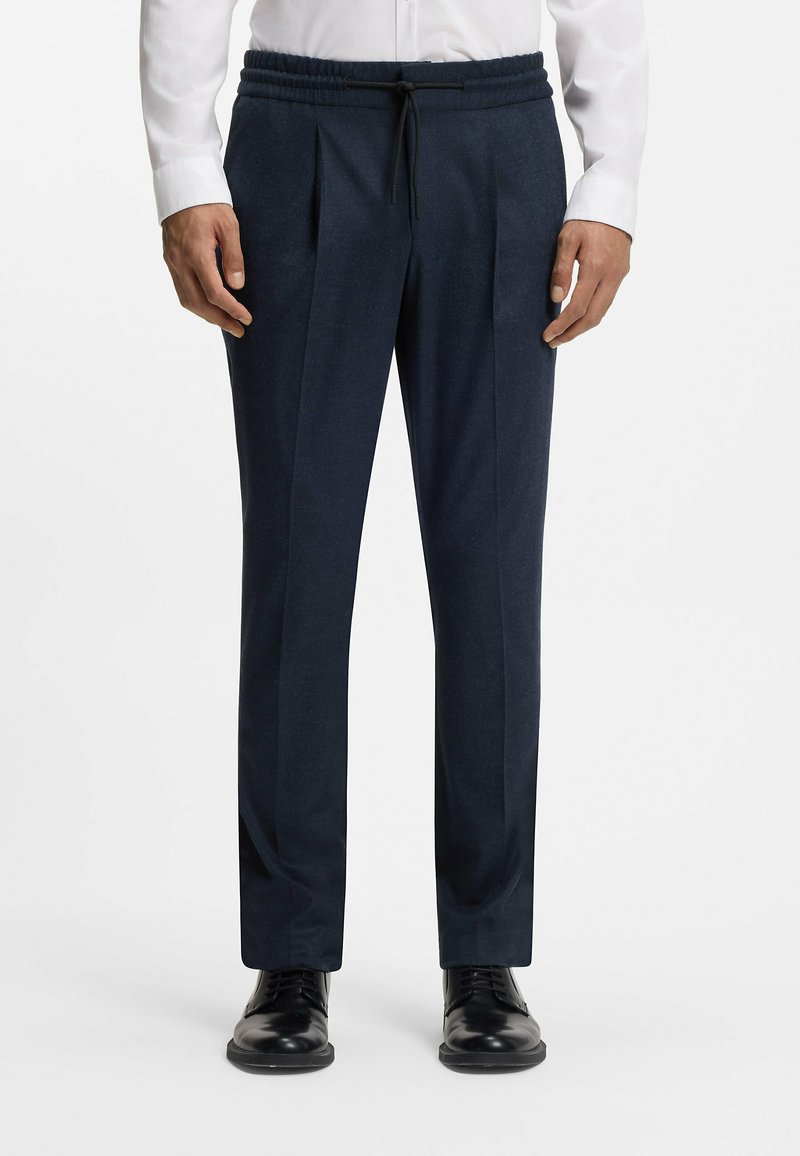 Pantaloni stretch blu navy con vestibilità comoda, caratterizzati da pince, una vita con coulisse e una texture liscia. Abbinati a scarpe in pelle nera.