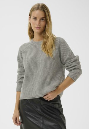 Grau gestrickter Pullover aus Rippstrick mit Rundhalsausschnitt und Raglanärmel, kombiniert mit einem schwarzen Lederrock, der eine lockere Passform und umgeschlagene Ärmelbündchen aufweist.
