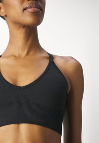 Top desportivo preto com um design em V, textura canelada na faixa e alças finas ajustáveis. Tecido suave com um formato ajustado.