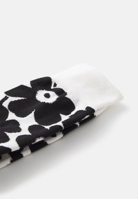 Calcetines con un patrón floral en blanco y negro y un puño acanalado. El diseño presenta grandes flores y una textura suave.