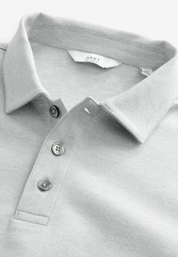 Polo gri, cu un material texturat, guler clasic, placket cu trei butoane și eticheta cu mărimea relaxată în interiorul gulerului.