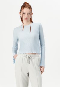 Haut bleu clair à manches longues avec une texture côtelée et un ourlet ondulé. Associé à un pantalon gris clair à cordon de serrage avec des coutures verticales.