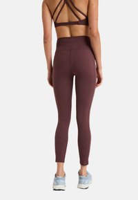 Leggings bordeaux taille haute avec une texture lisse, associés à un soutien-gorge de sport à dos strappy. Les chaussures sont des baskets de course bleu clair.