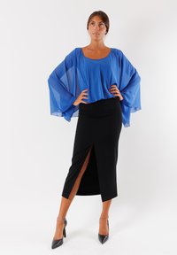 Top in chiffon blu con maniche a batwing abbinato a una gonna midi nera e aderente con uno spacco laterale, completato da tacchi neri.