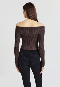 Dunkelbrauner, gerippter, schulterfreier Pullover mit langen Ärmeln, taillierter Silhouette und kurzer Länge, kombiniert mit hochgeschnittenen schwarzen Jeans.