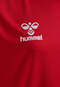 Rode sporttrui van glad, rekbaar materiaal. Bevat een witte Hummel-logo met gestileerd bijontwerp dat op de voorkant is geplaatst.