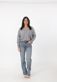 Maglione grigio chiaro lavorato a maglia con scollo a V e motivi a cuore dorati sparsi, abbinato a jeans a gamba dritta blu chiaro a vita alta.